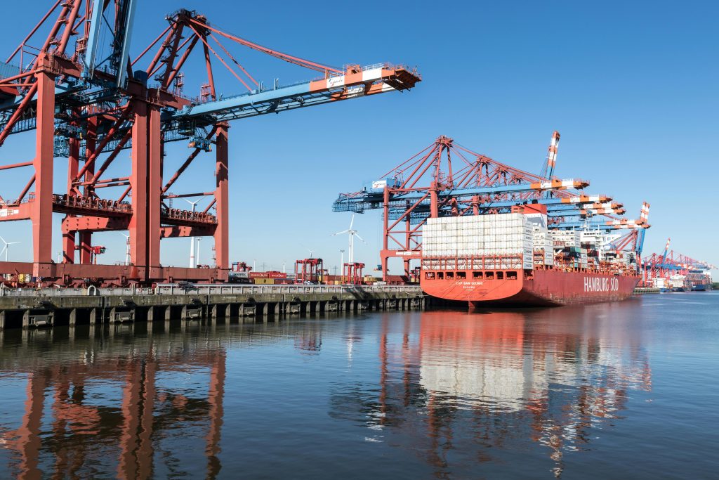 Container ship at Hamburg port with cranes on a clear day, showcasing industrial operations.